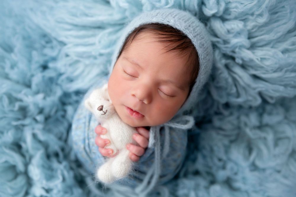 Peaceful newborn in blue knit wrap on matching textured backdrop.