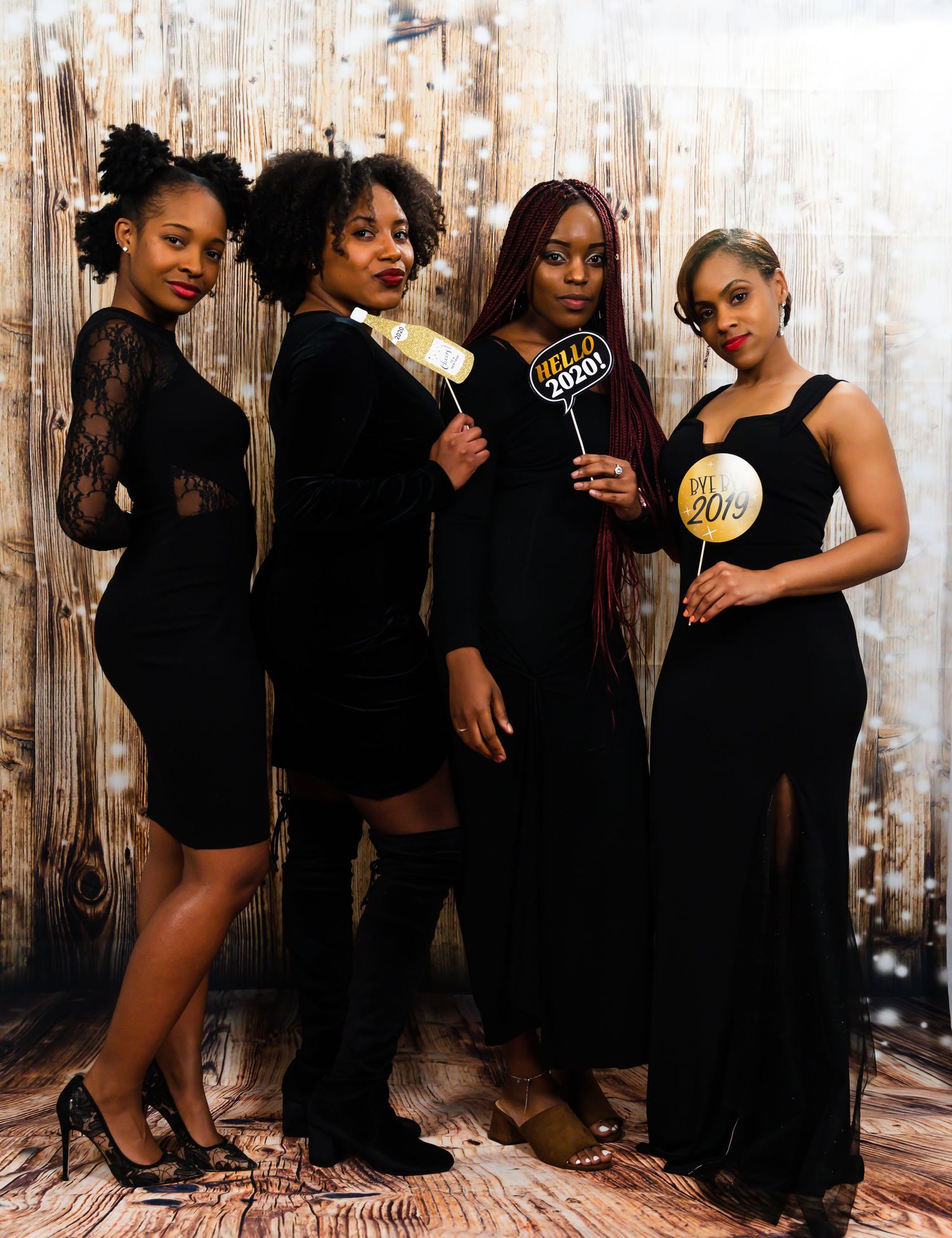 Four women in black dresses posing at New Year 2020 photo booth celebration.