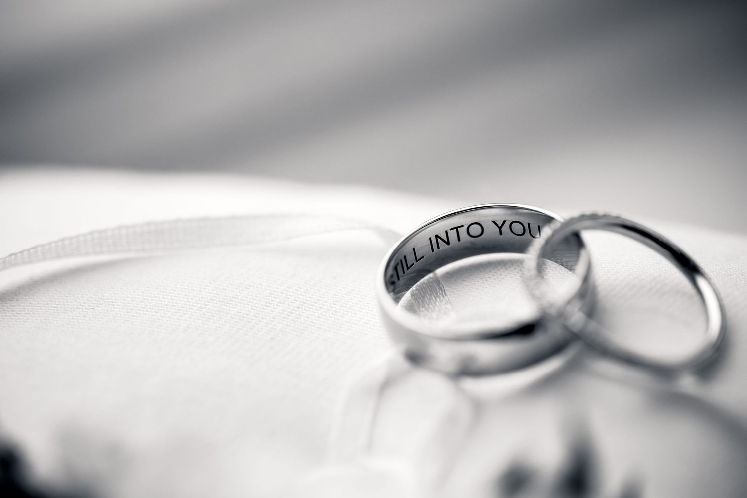 Two wedding rings with engraved text placed on white surface in black and white.