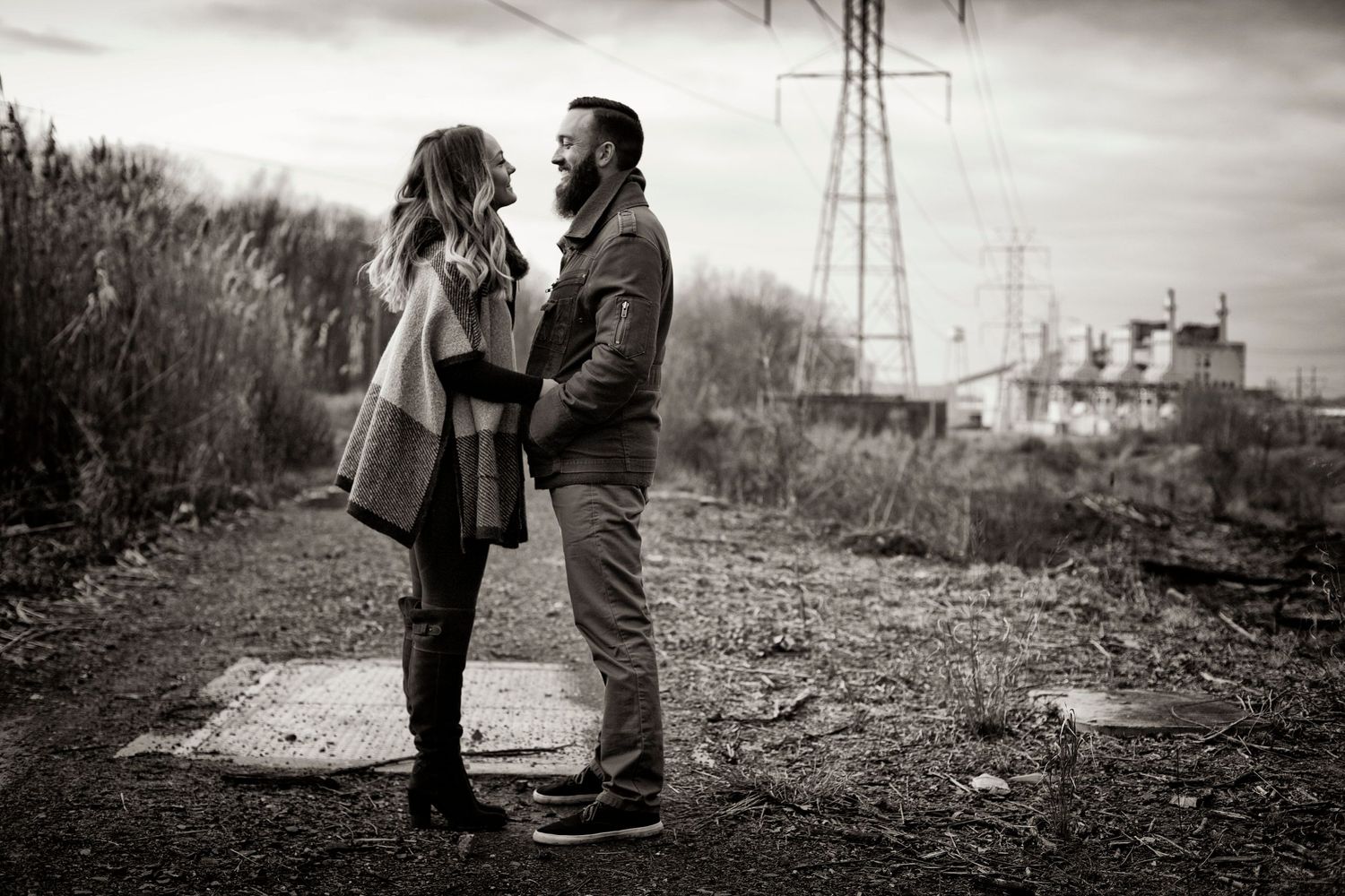 a couple are standing next to electricity poles near a river, in the style of industrial chic, matt wagner, blurry