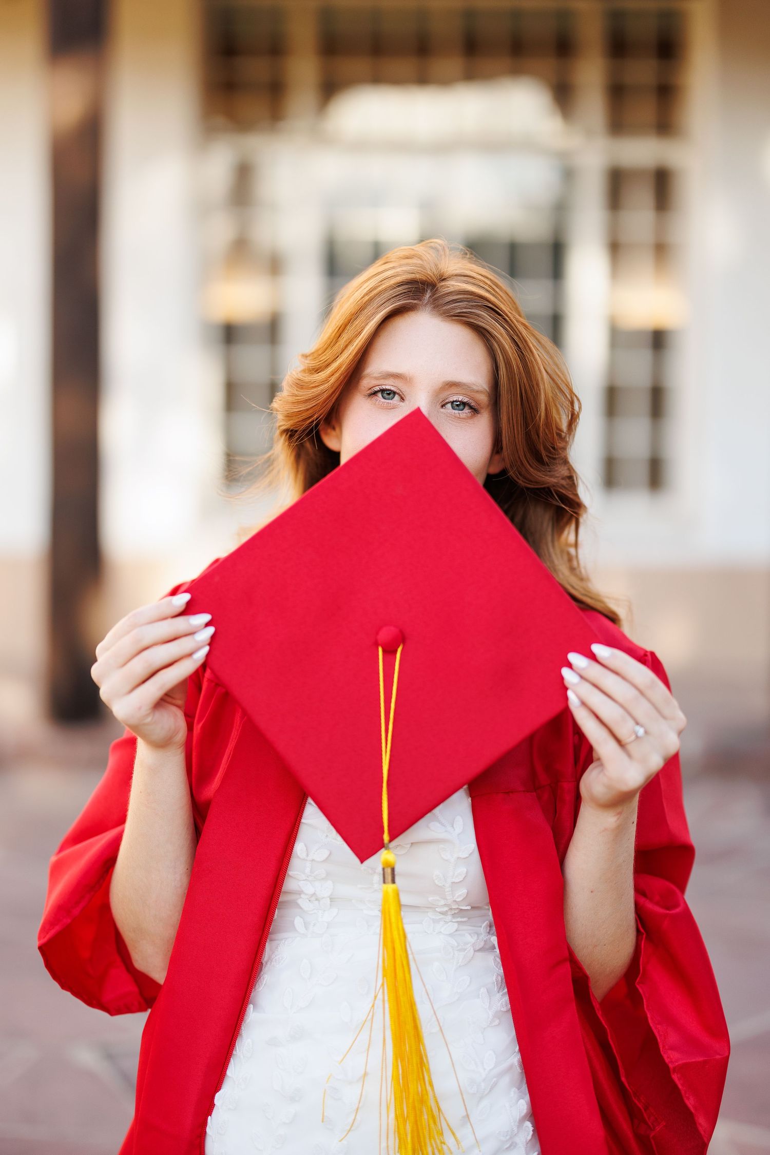 A graduation photo showing a red cap held up in front of white building columns.