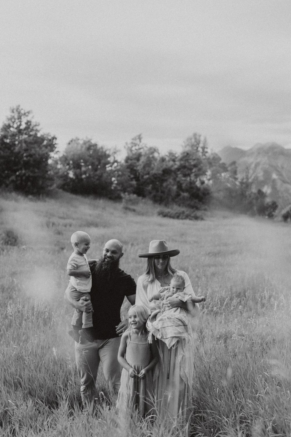 A black and white outdoor family portrait with a rustic mountain backdrop.