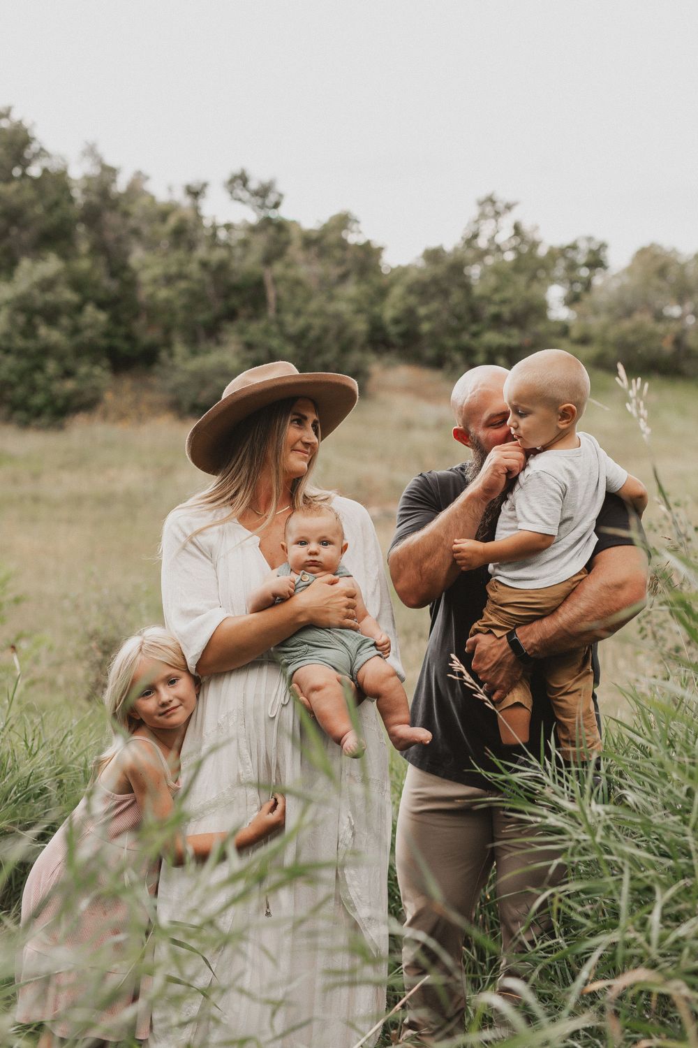 Family enjoying a candid moment together in a sunlit meadow with trees in the background.