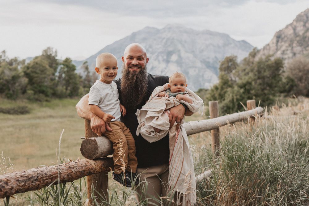 Family posing by a wooden fence with scenic mountain landscape behind them.