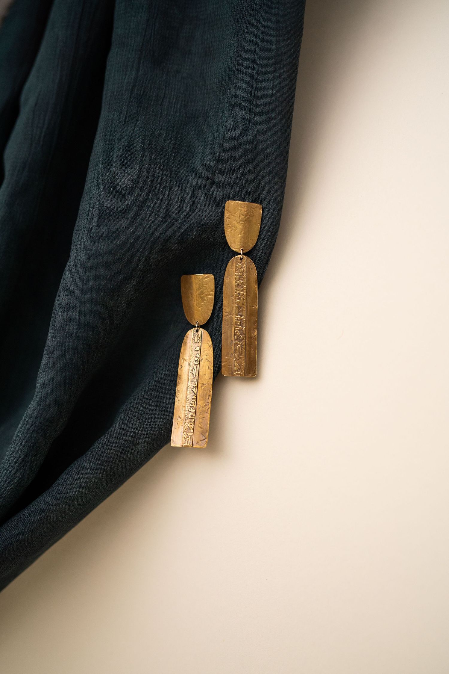 Sanetra Longno photo of Claire Sommers Buck Emerging Earrings in Oxidized brass dangling on a dark blue fabric