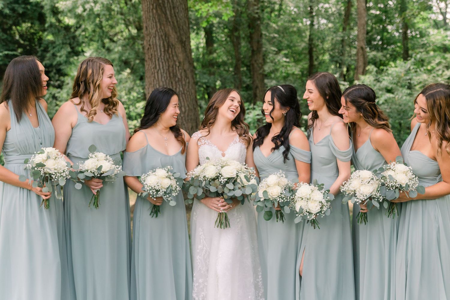 Wedding party lined up outdoors holding matching white floral bouquets.