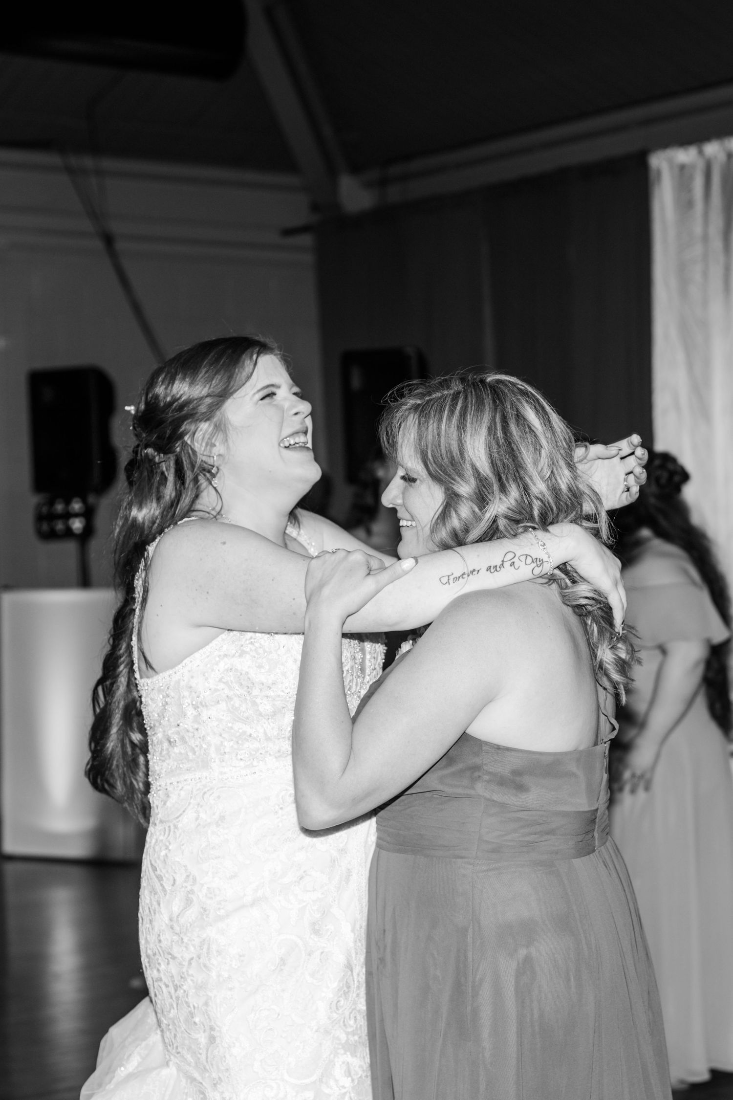 Emotional embrace between bride in white dress and bridesmaid in gray during wedding reception.