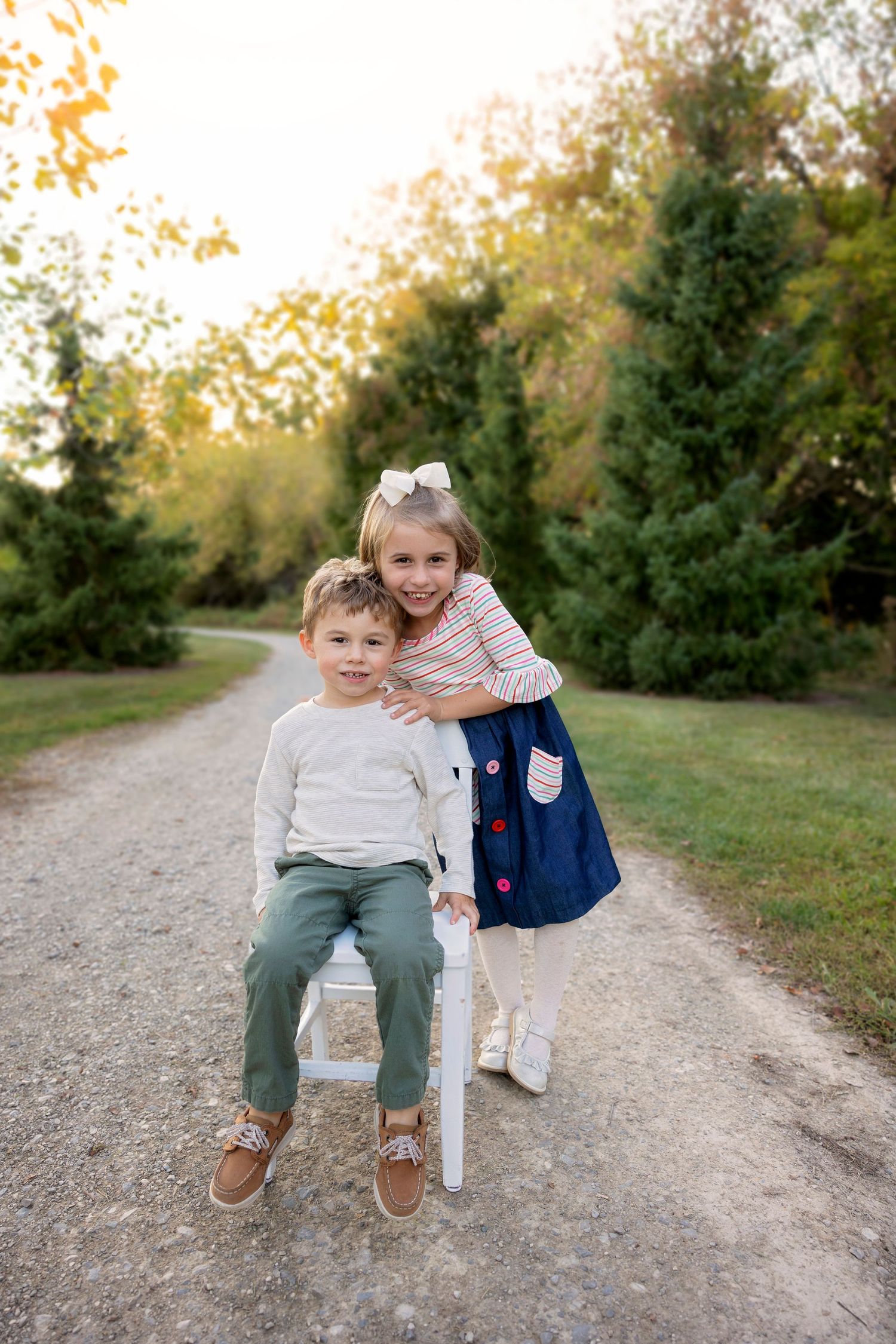 Two children share a sweet moment together on a dirt path surrounded by evergreen trees.