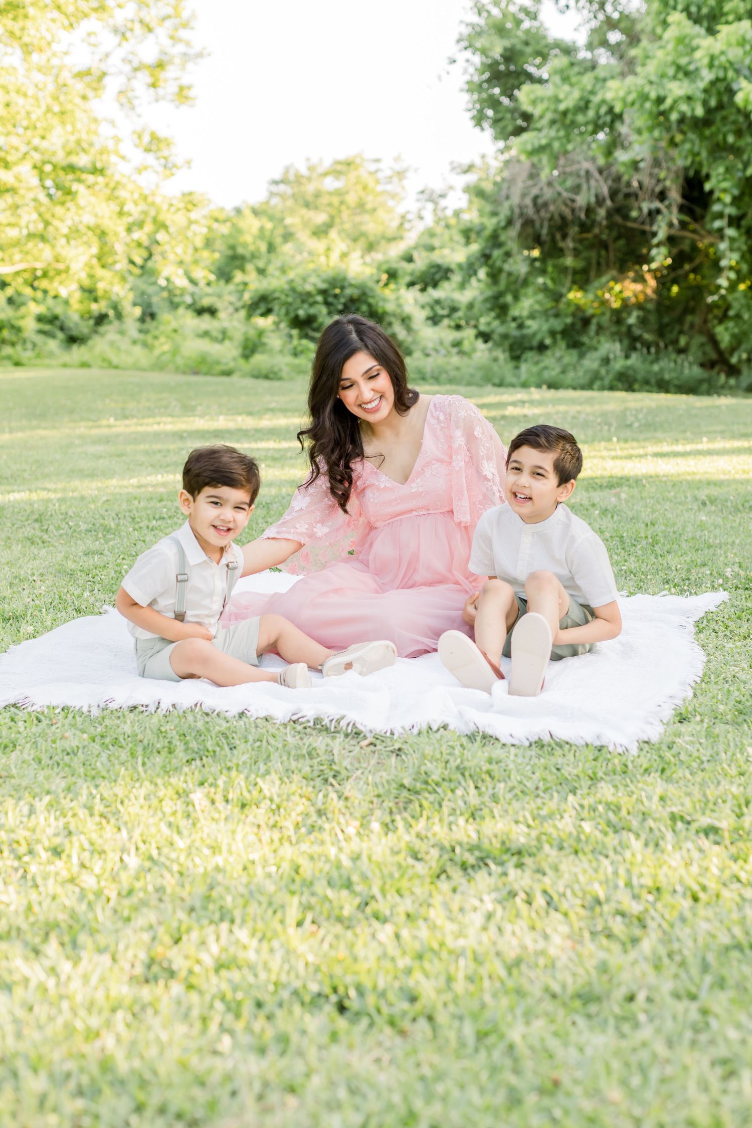 A joyful outdoor family moment captured on a white blanket in a sunny park setting.