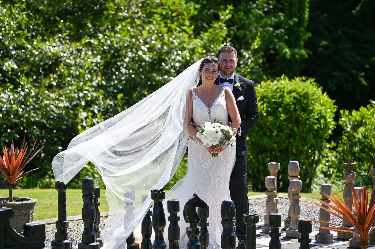 Couple poses by ornate railings as bride's veil flows dramatically in the breeze.