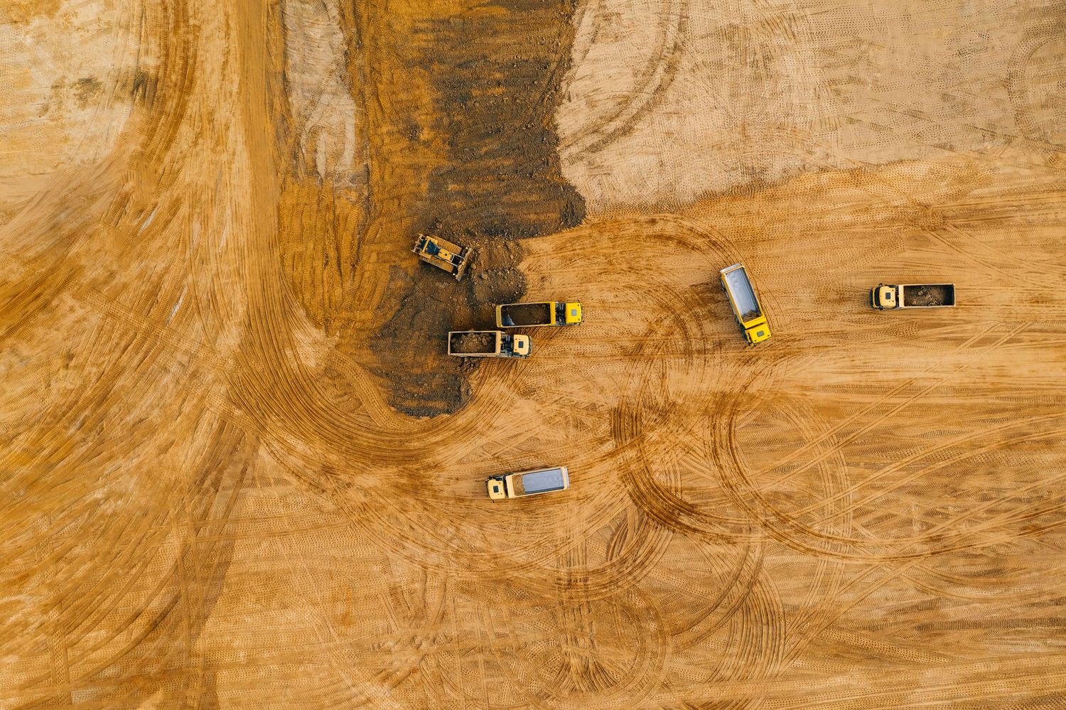 Bird's eye view of construction vehicles operating on dusty brown terrain.