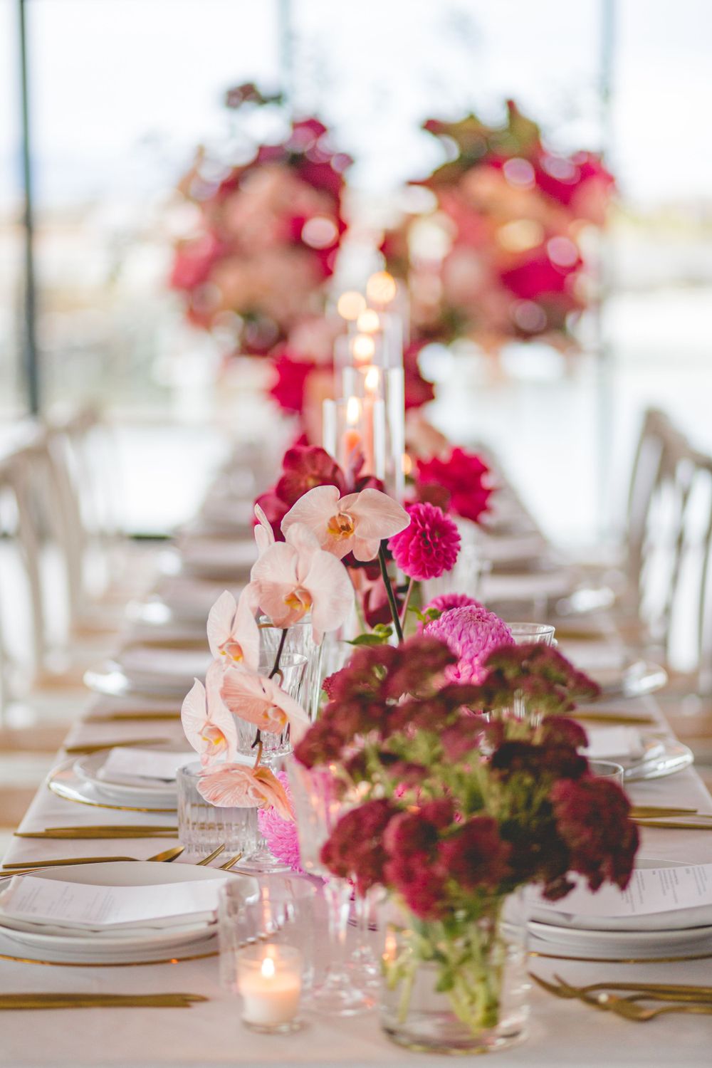 Intimate table setting with pink orchids, roses and glowing candles in glass vessels.