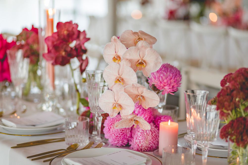 Elegant place setting with pink orchids, carnations and lit candles on white tablecloth.