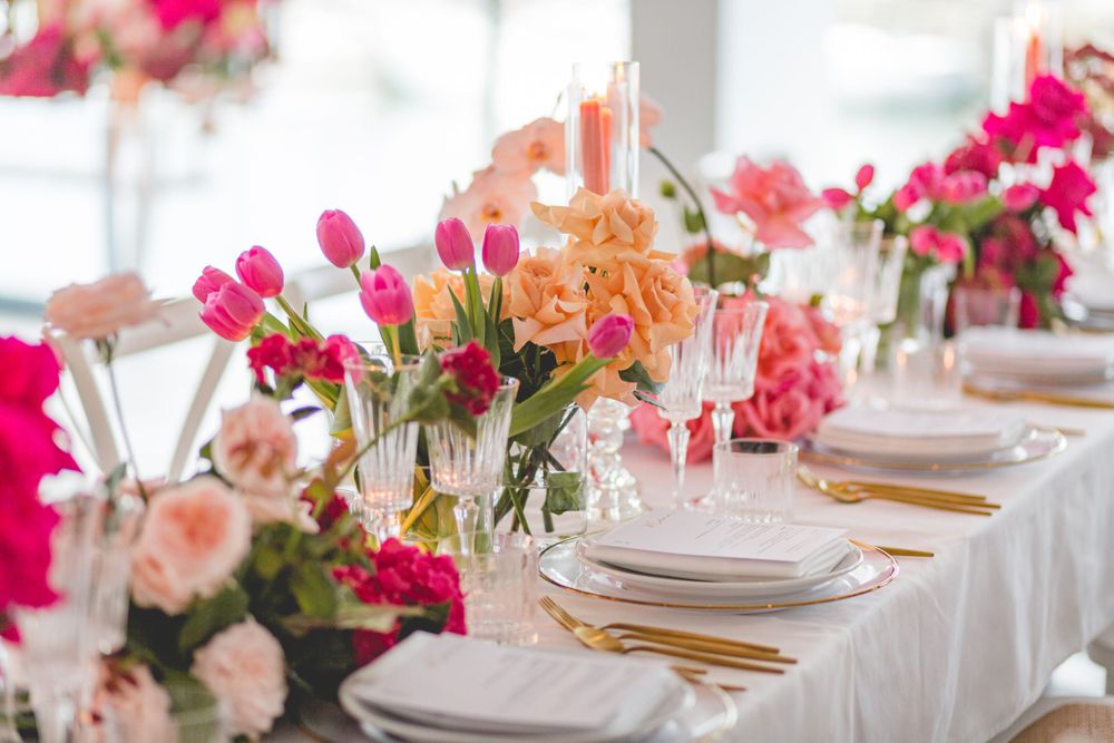 Luxurious table setting with vibrant pink and coral floral arrangements and gold flatware.