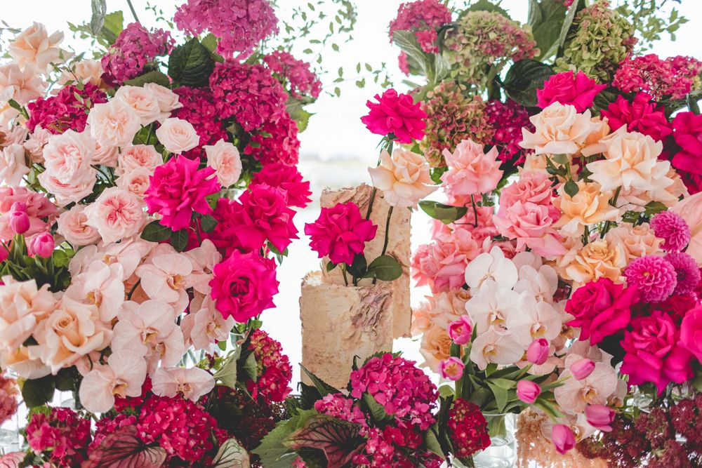 Luxurious floral arrangement featuring vibrant pink roses and soft peach orchids against a white background.