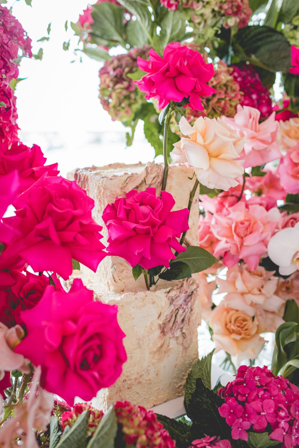 Elegant floral display with bright fuchsia roses and pale pink blooms around a textured vase.