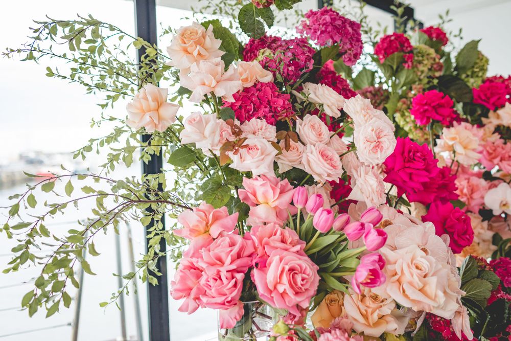 Cascading pink and peach floral arrangement with roses and greenery near large windows.