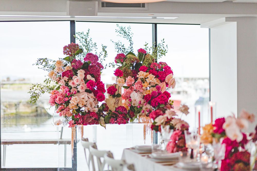 Elegant reception table setup with dramatic pink floral centerpieces and window views.