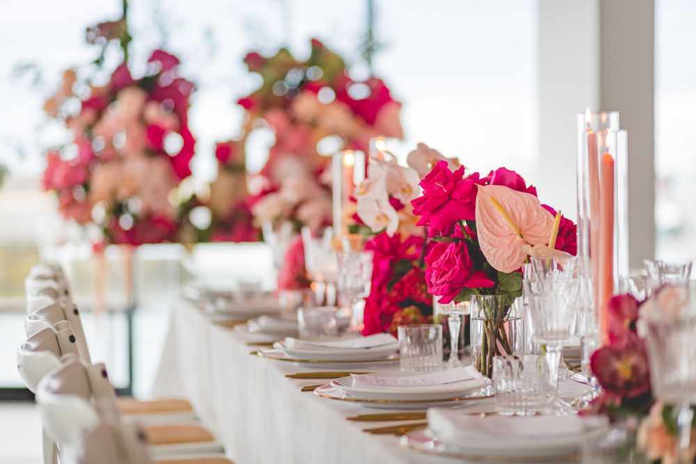 Long white dining table with pink floral arrangements and place settings for an elegant event.