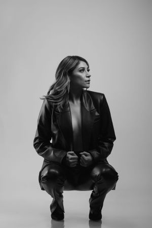 Dramatic black and white portrait of woman in leather jacket crouching.