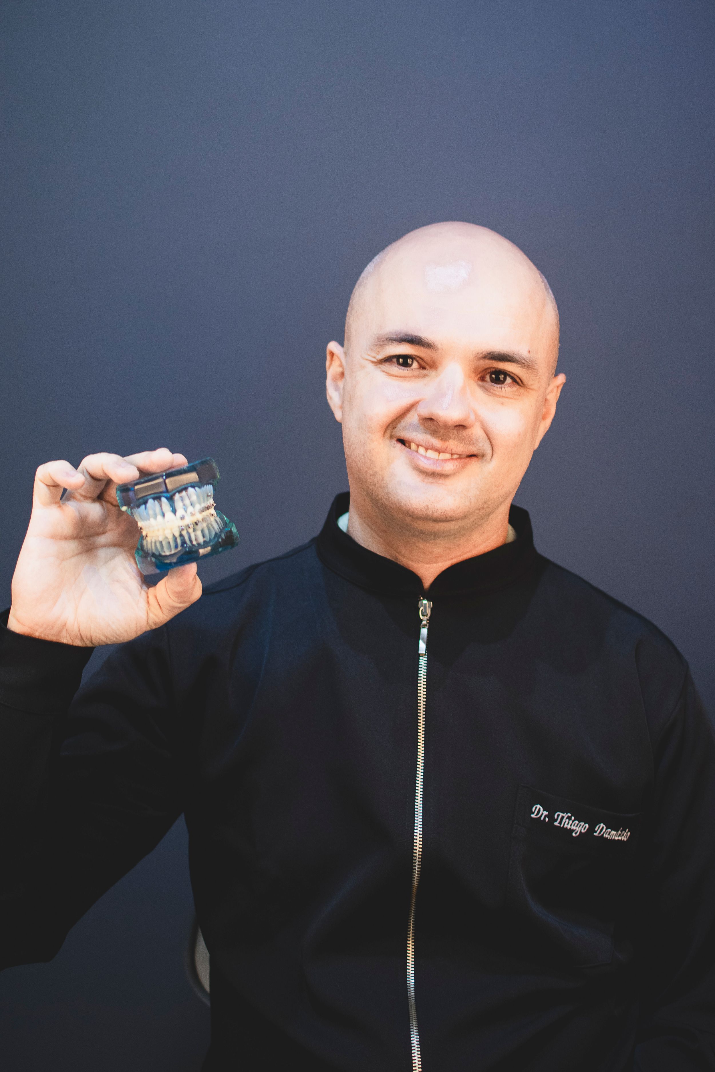 Healthcare professional in black jacket showing dental model against blue background.