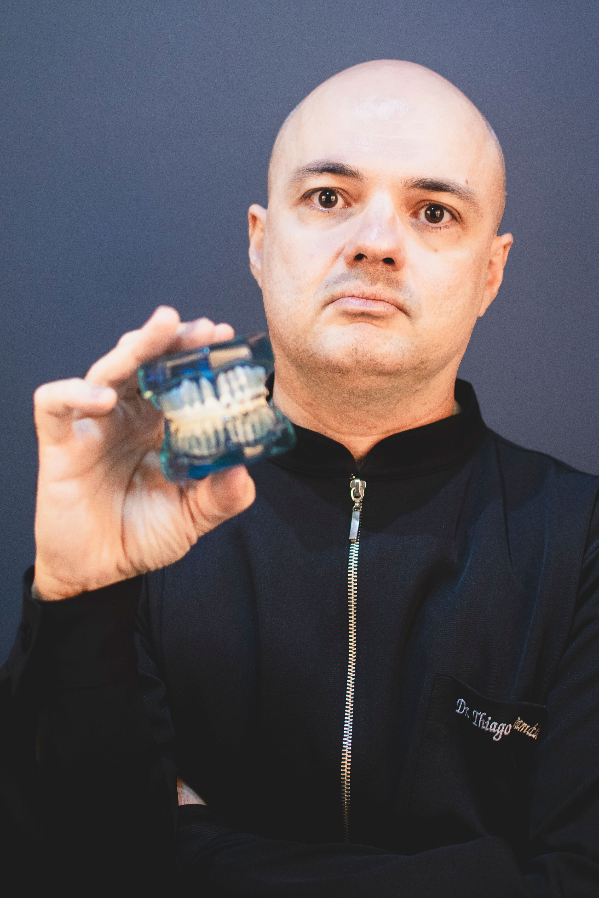 Medical professional displaying dental model while wearing black uniform against dark backdrop.