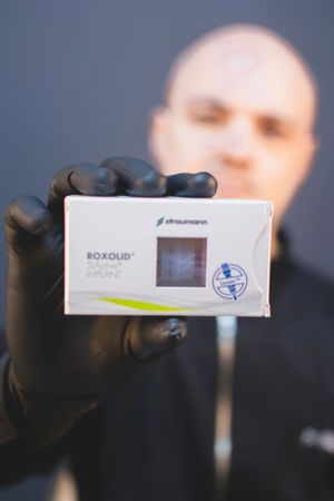 Hand in black glove holding Roxolid medical product box against blurred background.