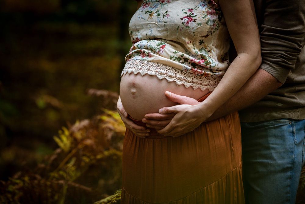 Detailfoto van zwangere buik met handen in herfstsfeer – zwangerschapsfotografie Arnhem