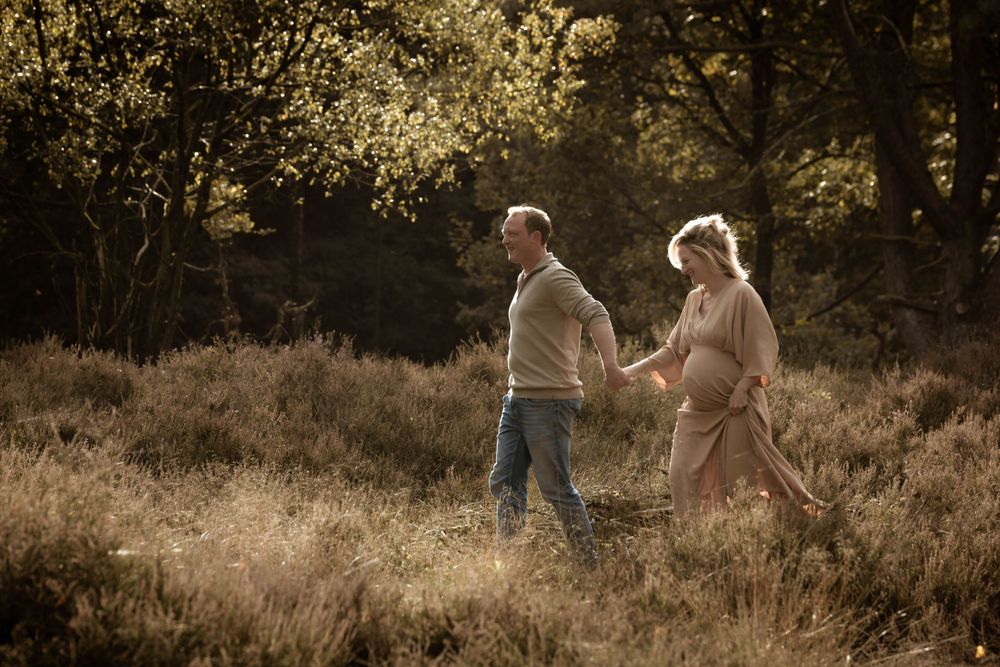 Zwanger koppel loopt hand in hand over de heide – zwangerschapsfotoshoot op de Veluwe