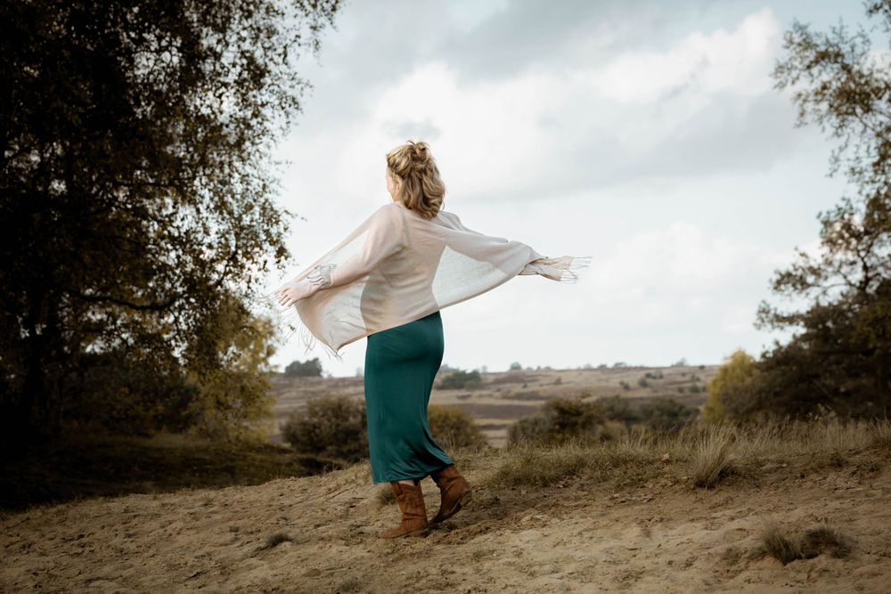Stralende zwangere vrouw in turquoise jurk draait een pirouette in het zand op de Veluwe – zwangerschapsfotografie Gelderland