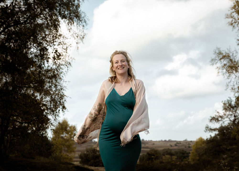 Stralende zwangere vrouw in turquoise jurk wandelt over de Veluwe – zwangerschapsfotoshoot Gelderland