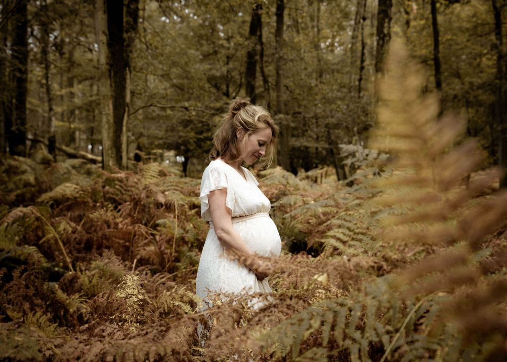 Zwangere vrouw in witte jurk tussen bruine varens – zwangerschapsfotoshoot in het bos