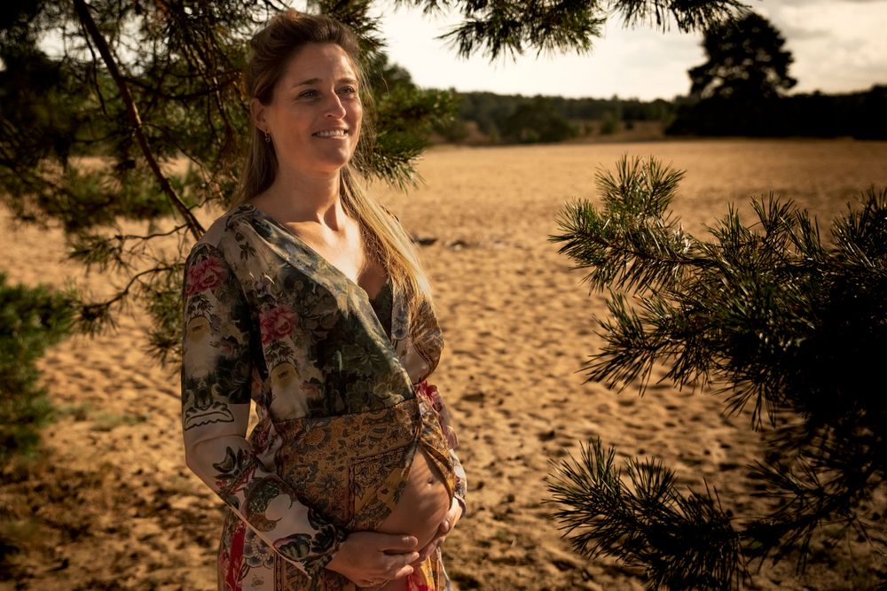 Lachende zwangere vrouw in een jurk met warme kleuren in de natuur op de Veluwe – zwangerschapsfotografie 
Gelderland