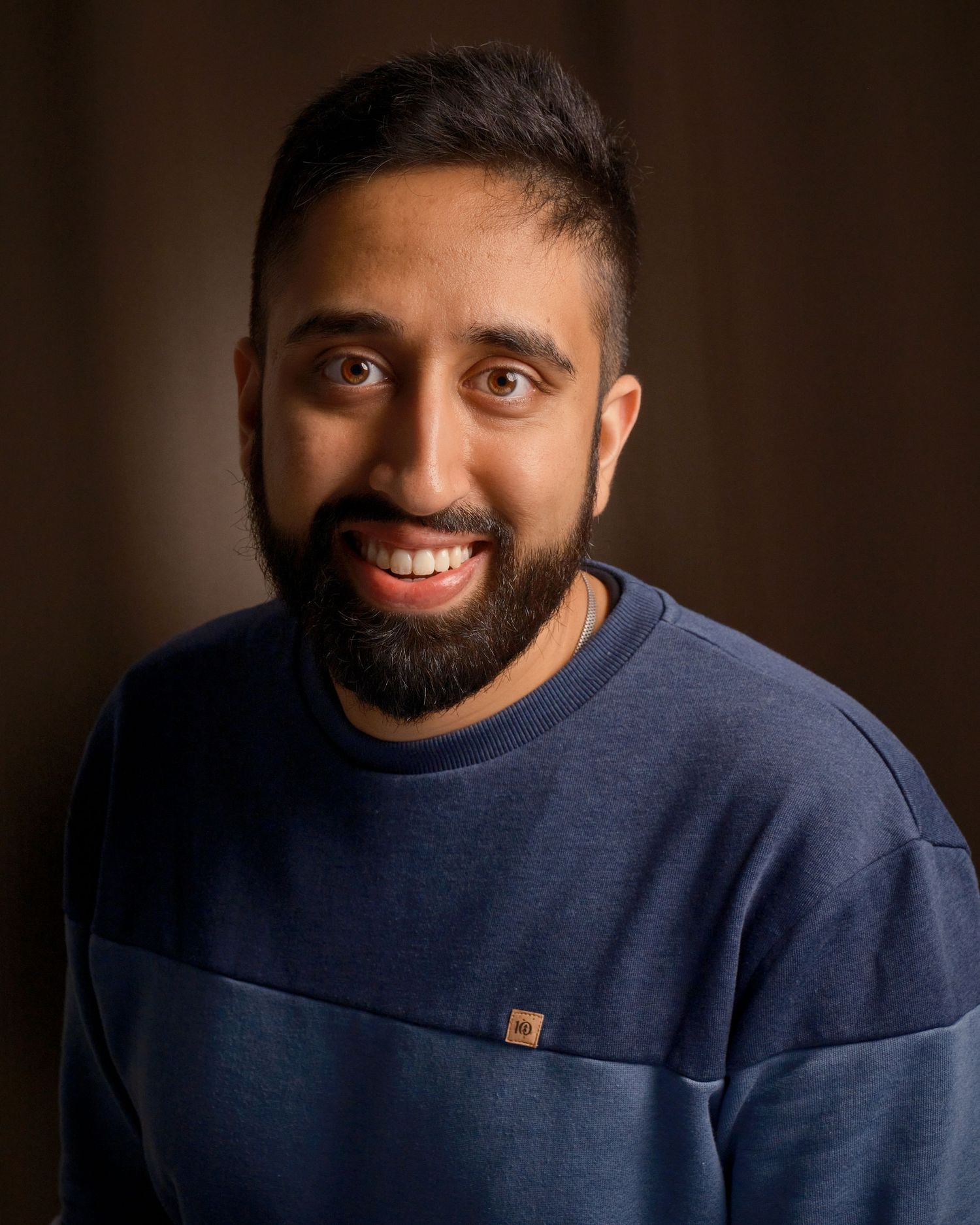 Portrait of person in navy sweater smiling against dark brown backdrop.