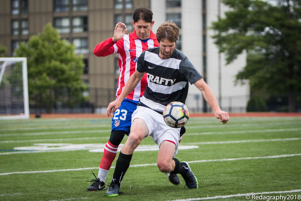 Two soccer players competing for ball, one in red stripes and one in black Drafty jersey.