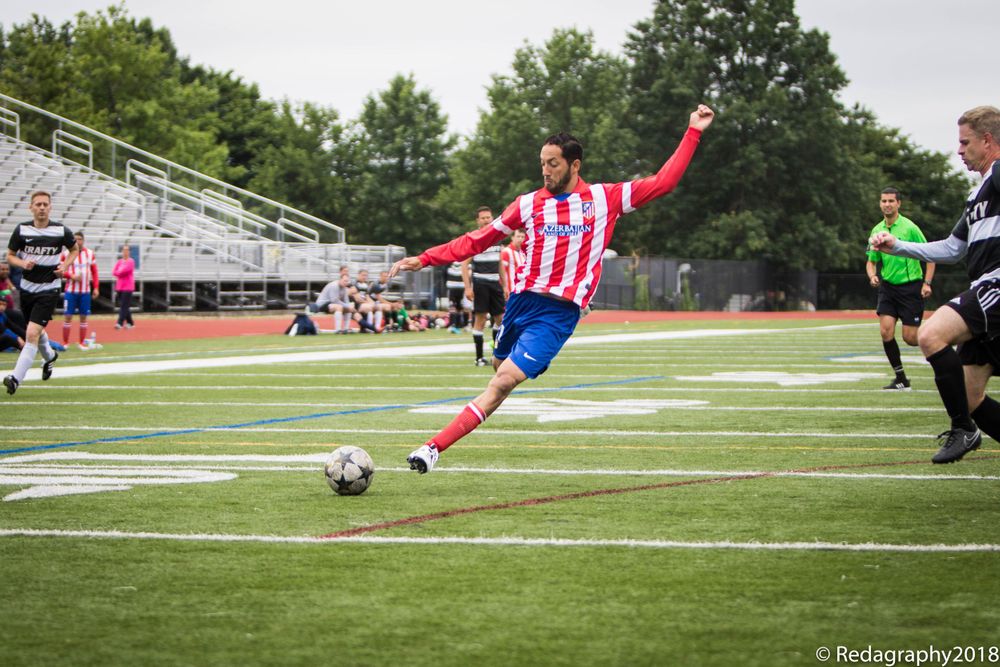 Soccer player in red and white uniform kicking the ball during a competitive outdoor game.