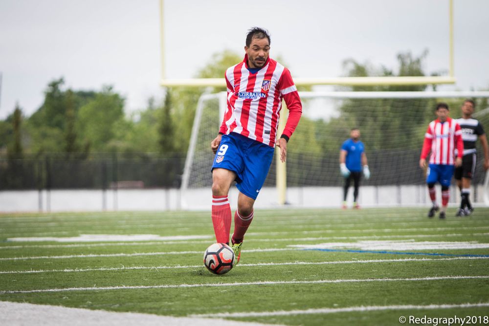 Soccer player in red and white striped jersey dribbling the ball during an outdoor match.