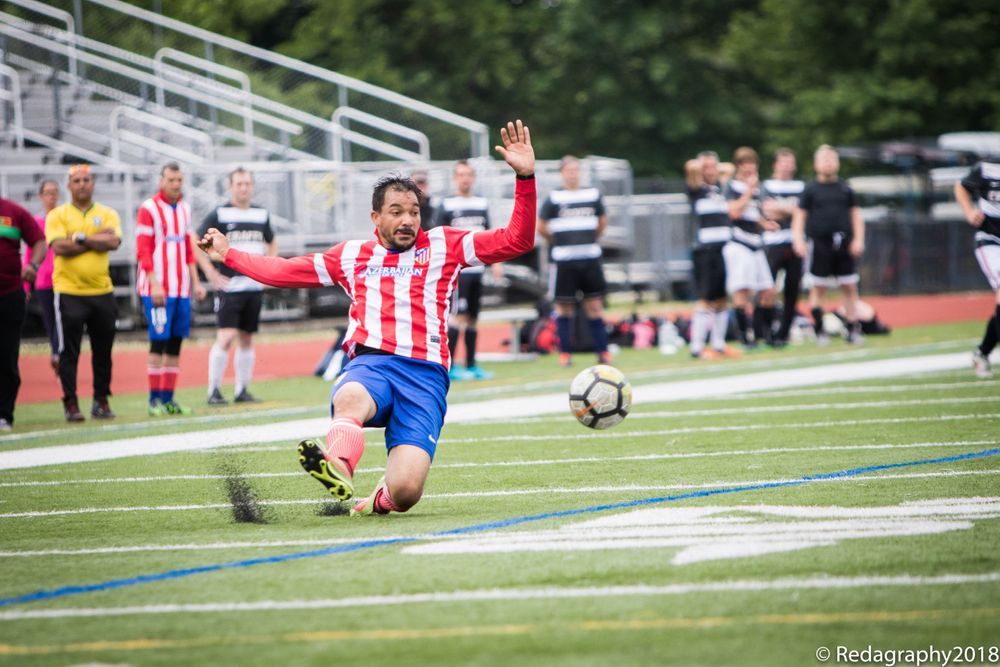 Soccer player in red and white striped jersey sliding on green turf field during competitive match.