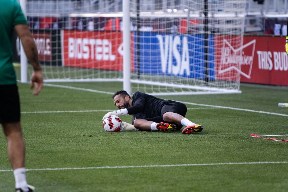 Goalkeeper in black uniform making a diving save during soccer practice on turf field.