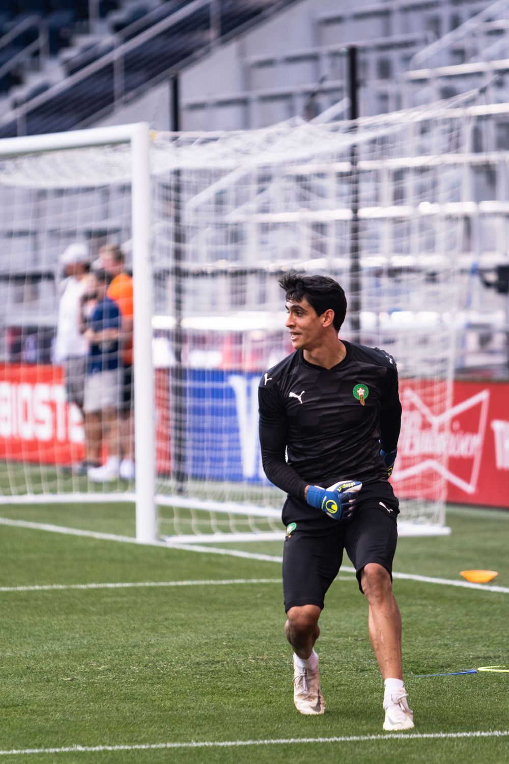 Soccer goalkeeper in black uniform warming up on green field in front of goal net.