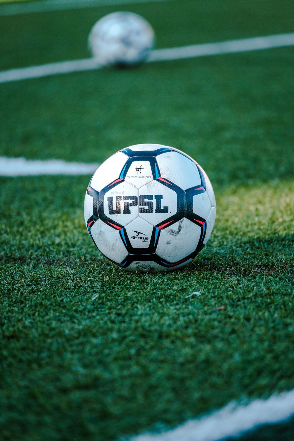 UPSL branded soccer ball on green turf field with second ball visible in background.