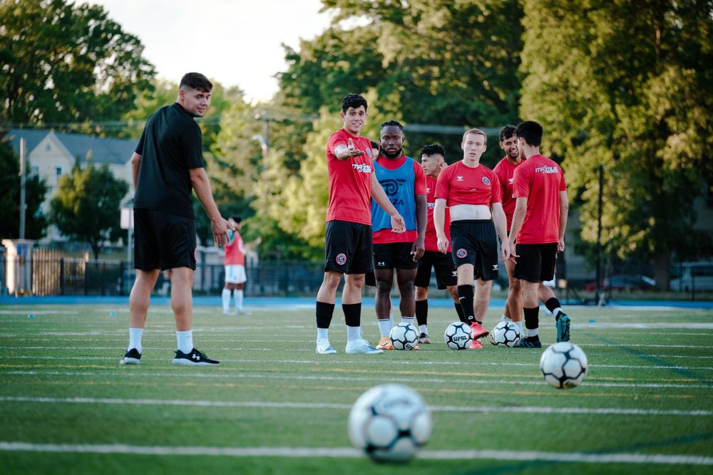 Soccer coach instructing group of players in red uniforms during outdoor training session.