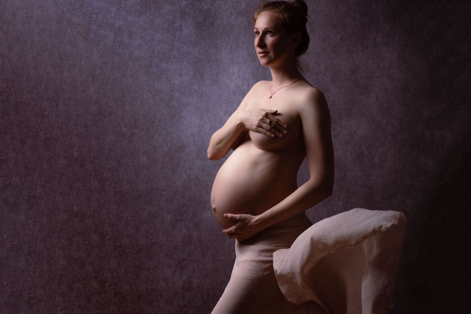 Elegant maternity portrait of smiling pregnant woman posing in studio with soft purple backdrop.