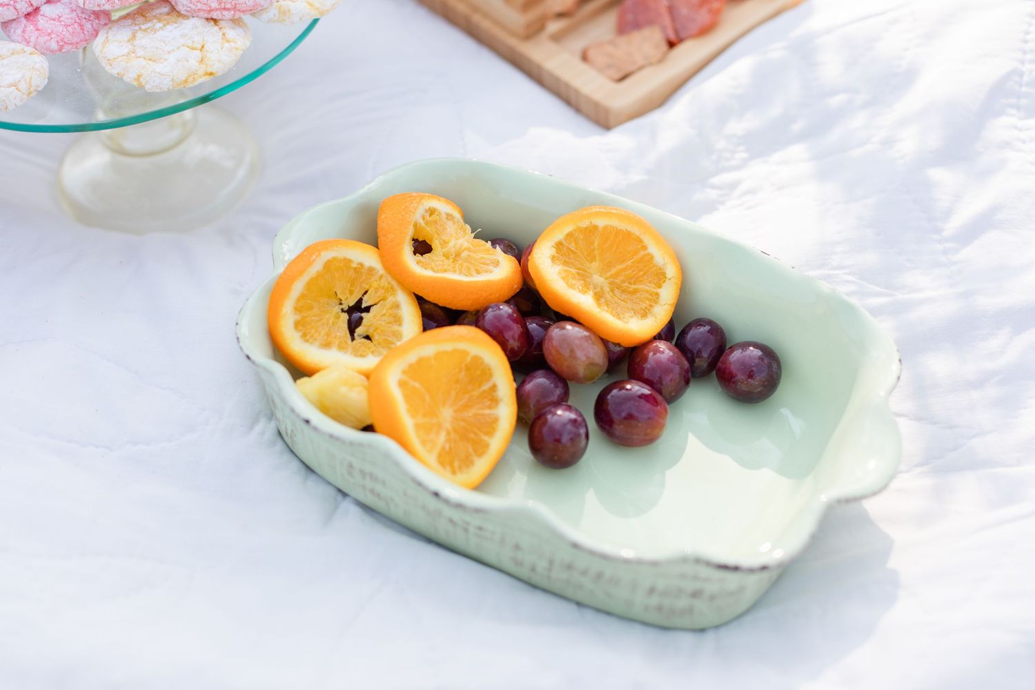 Fresh oranges and grapes arranged on a mint green ceramic serving plate.