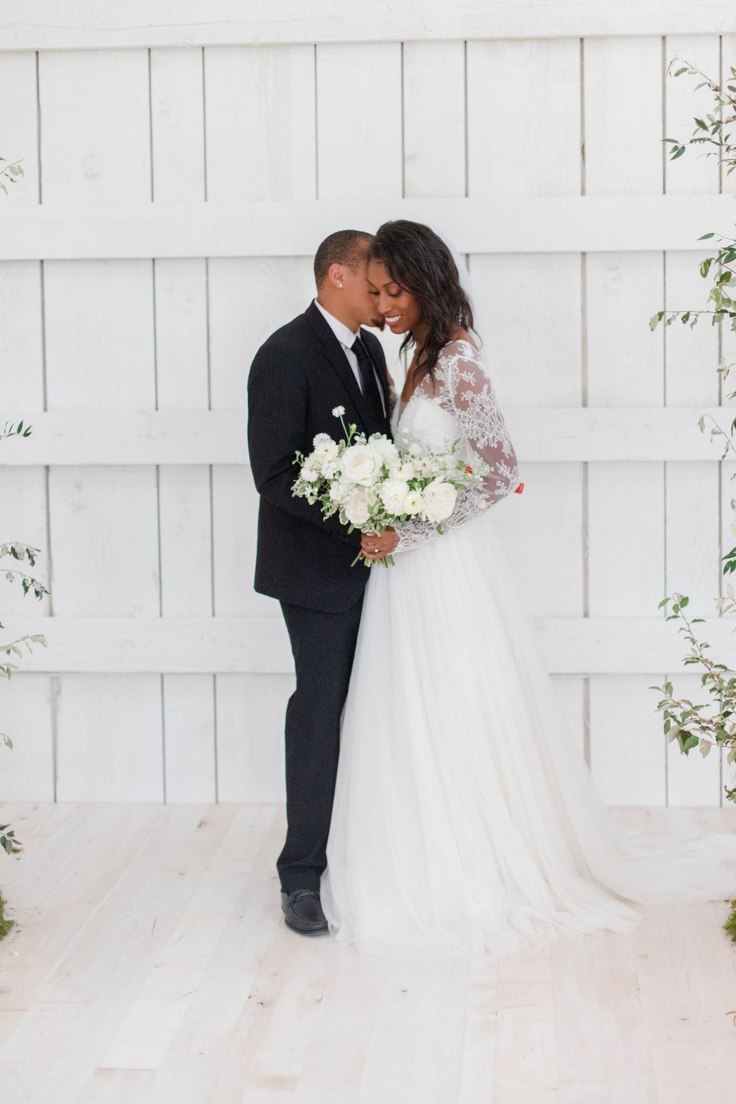 Wedding couple sharing a tender moment against white wooden paneled backdrop.