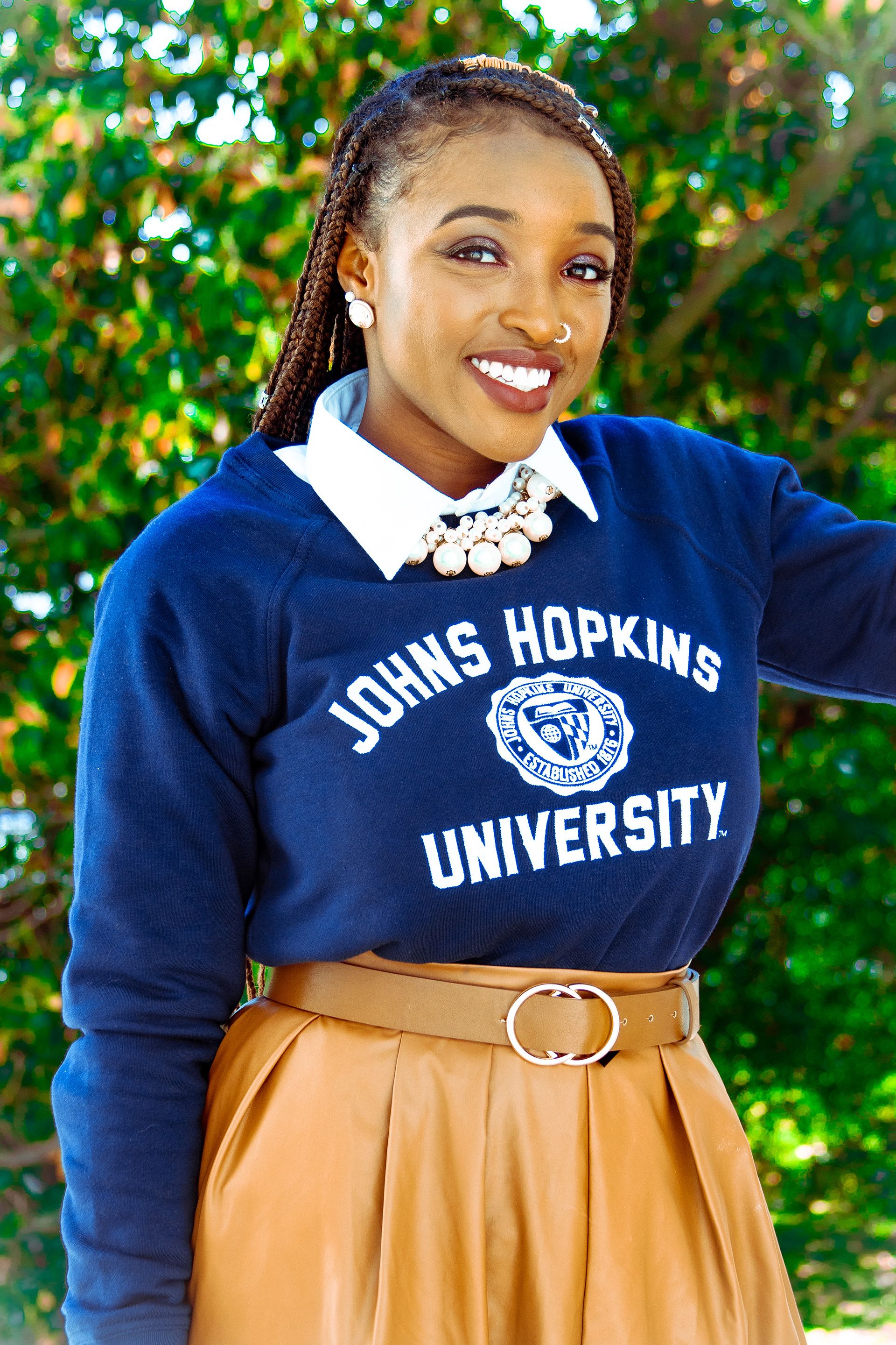 Person wearing Johns Hopkins University navy sweater and tan skirt poses in outdoor setting.