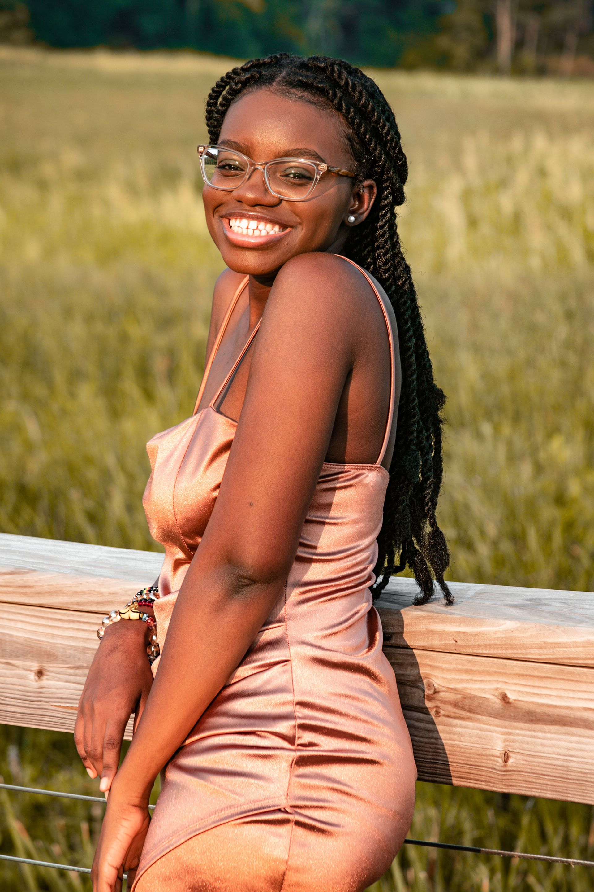 Person in pink dress poses on wooden fence during golden hour outdoor photoshoot.