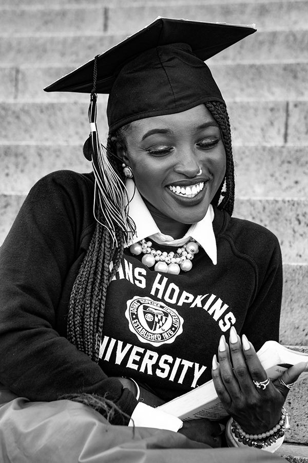 A graduate in cap and gown smiles while looking down at a Johns Hopkins University sweatshirt.