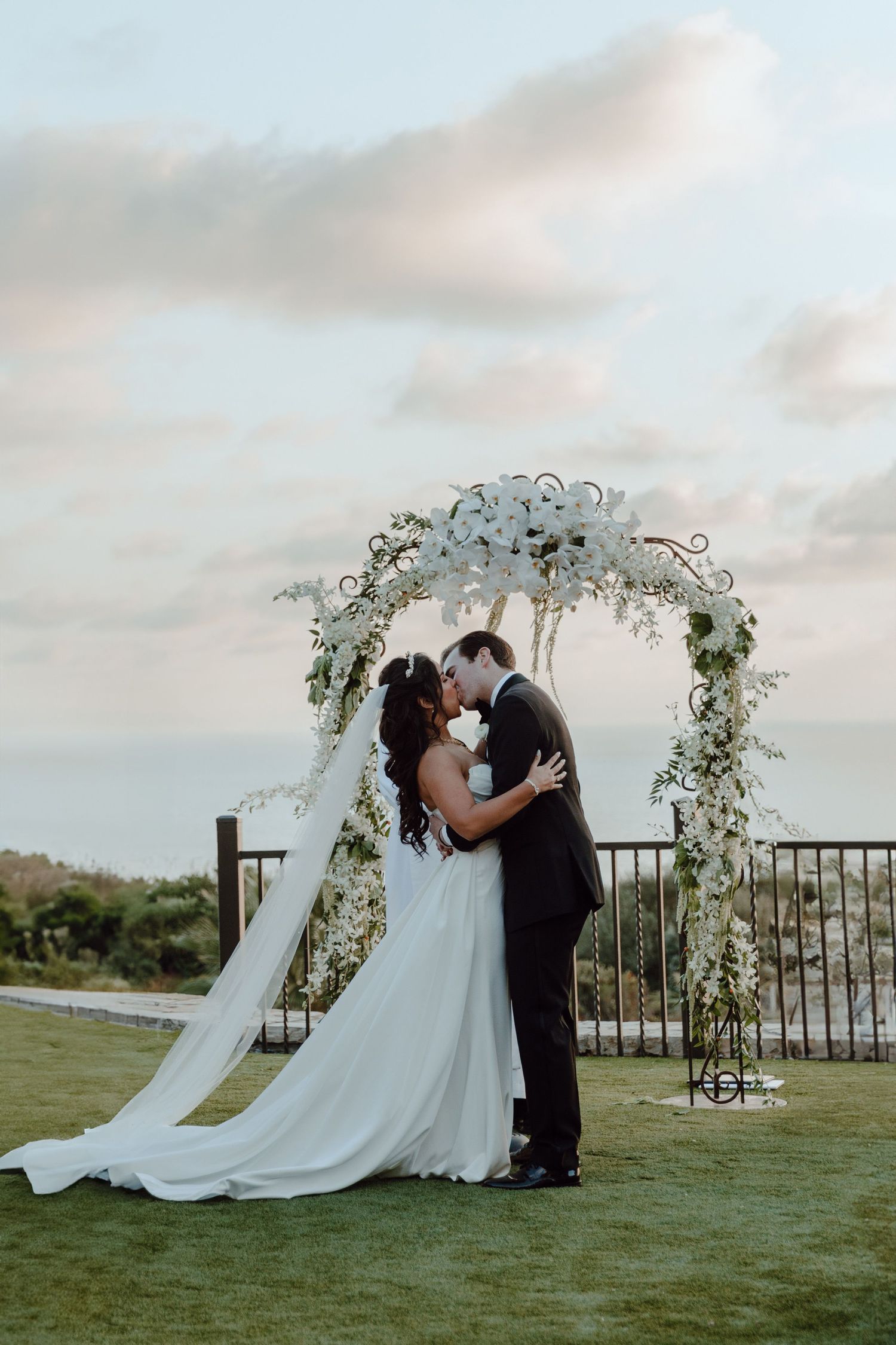 Married couple shares their first kiss as husband and wife. They stand in front of their beautiful floral alter.
