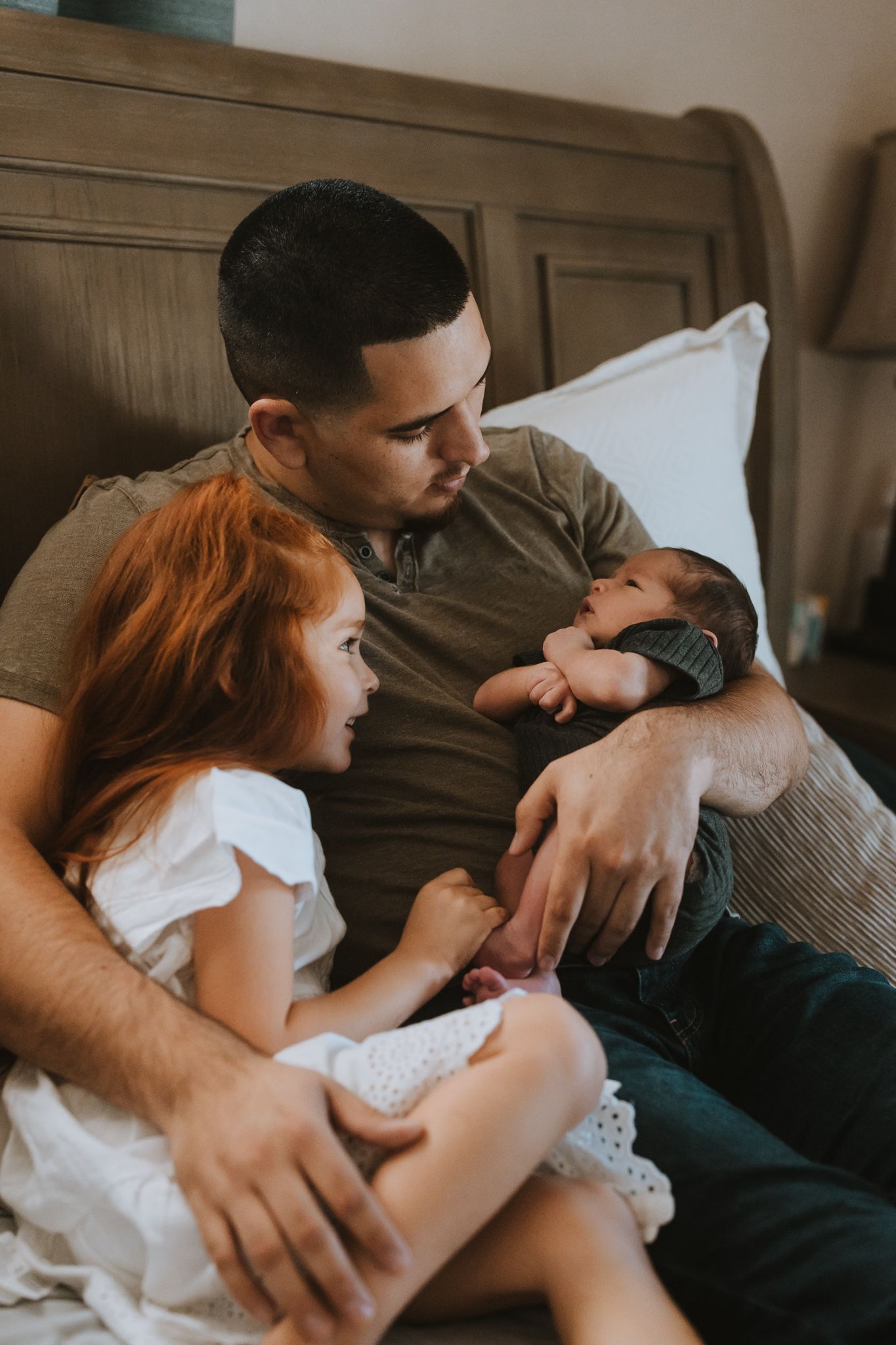A tender family moment showing a father holding a newborn baby while sitting with a young child in casual attire.